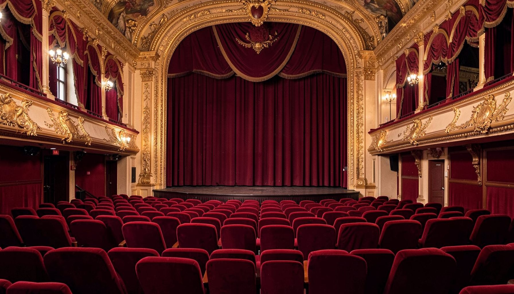 A European variety theater interior with red plush seats and gilded proscenium arch, rich crimson and gold tones, late-Edwardian elegance