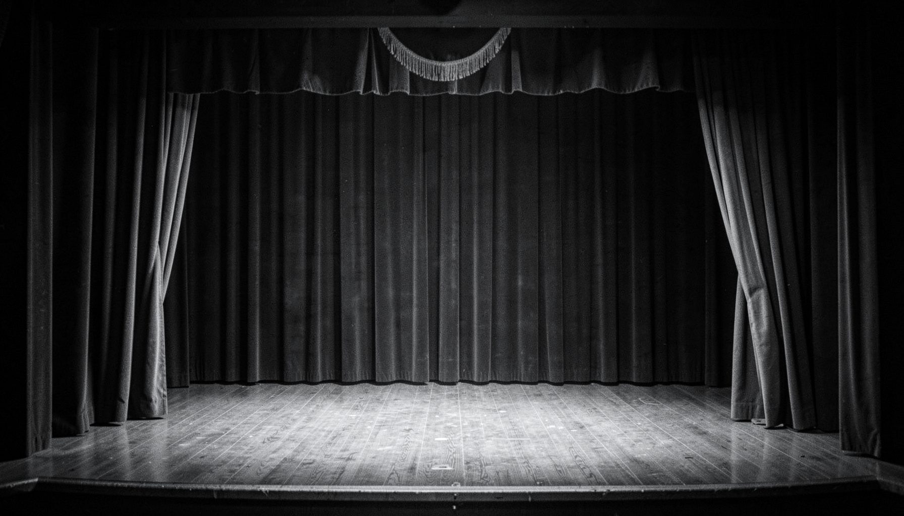 A softly lit black-and-white vaudeville stage with velvet curtains drawn back, muted silver and charcoal tones, suggesting an intimate early-1900s theater setting