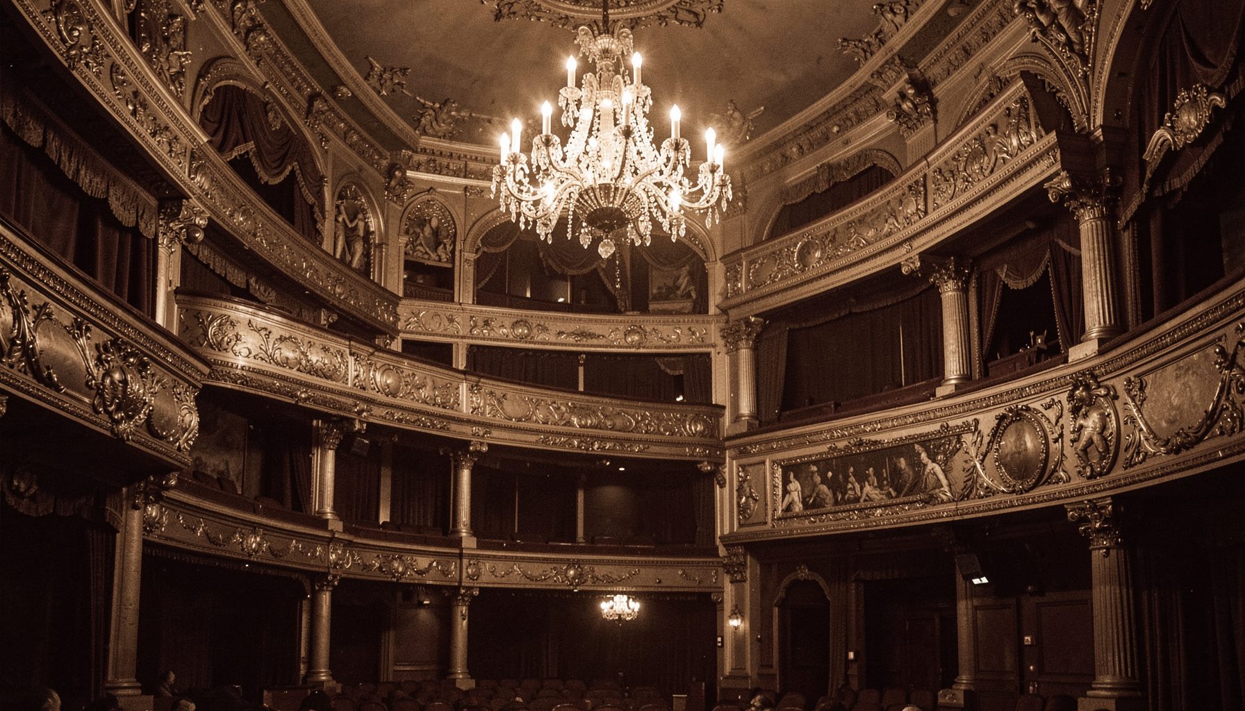 A vintage sepia-toned theater interior with ornate gilded balconies and a grand chandelier, warm amber and deep brown tones, evoking an early-20th-century Broadway playhouse